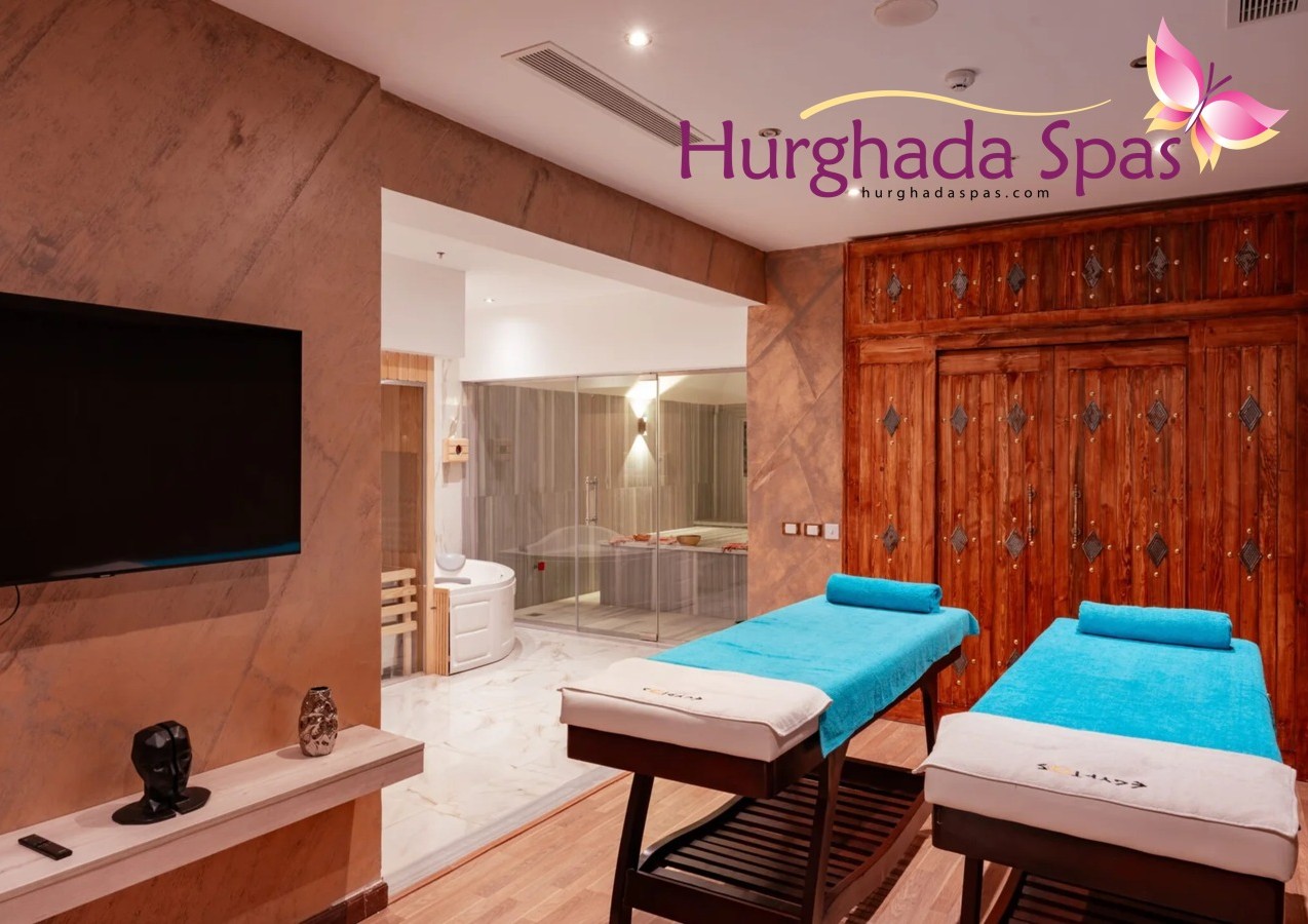 Interior of Egyptos Spa treatment room featuring two turquoise massage beds, a large wooden door, and a glass-enclosed Turkish bath steam room in the background.