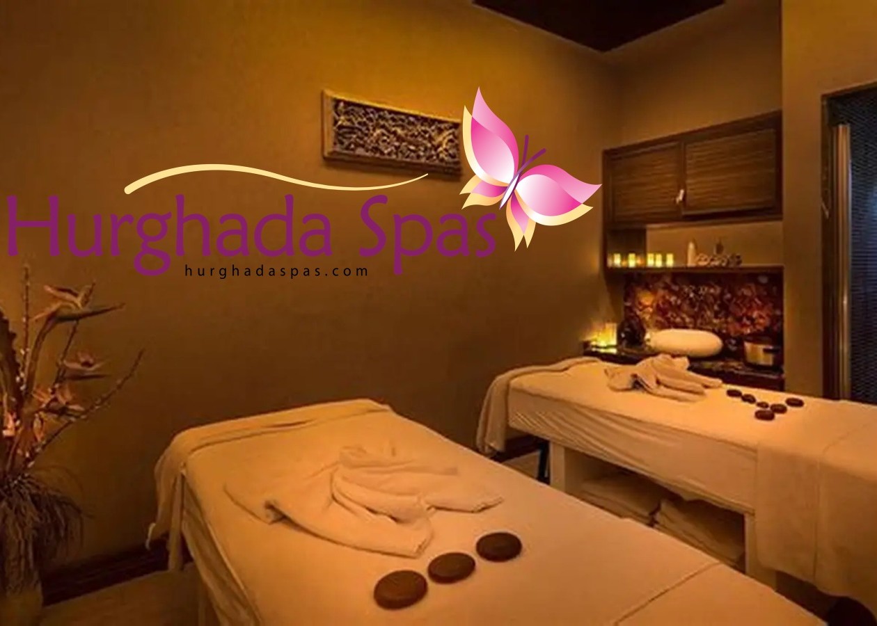 Two luxury massage tables prepared with hot stones and folded towels in a relaxing, dimly lit therapeutic wellness room.